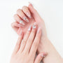 Hands with long, nude pink press-on nails featuring rhinestone and 3D floral nail art.