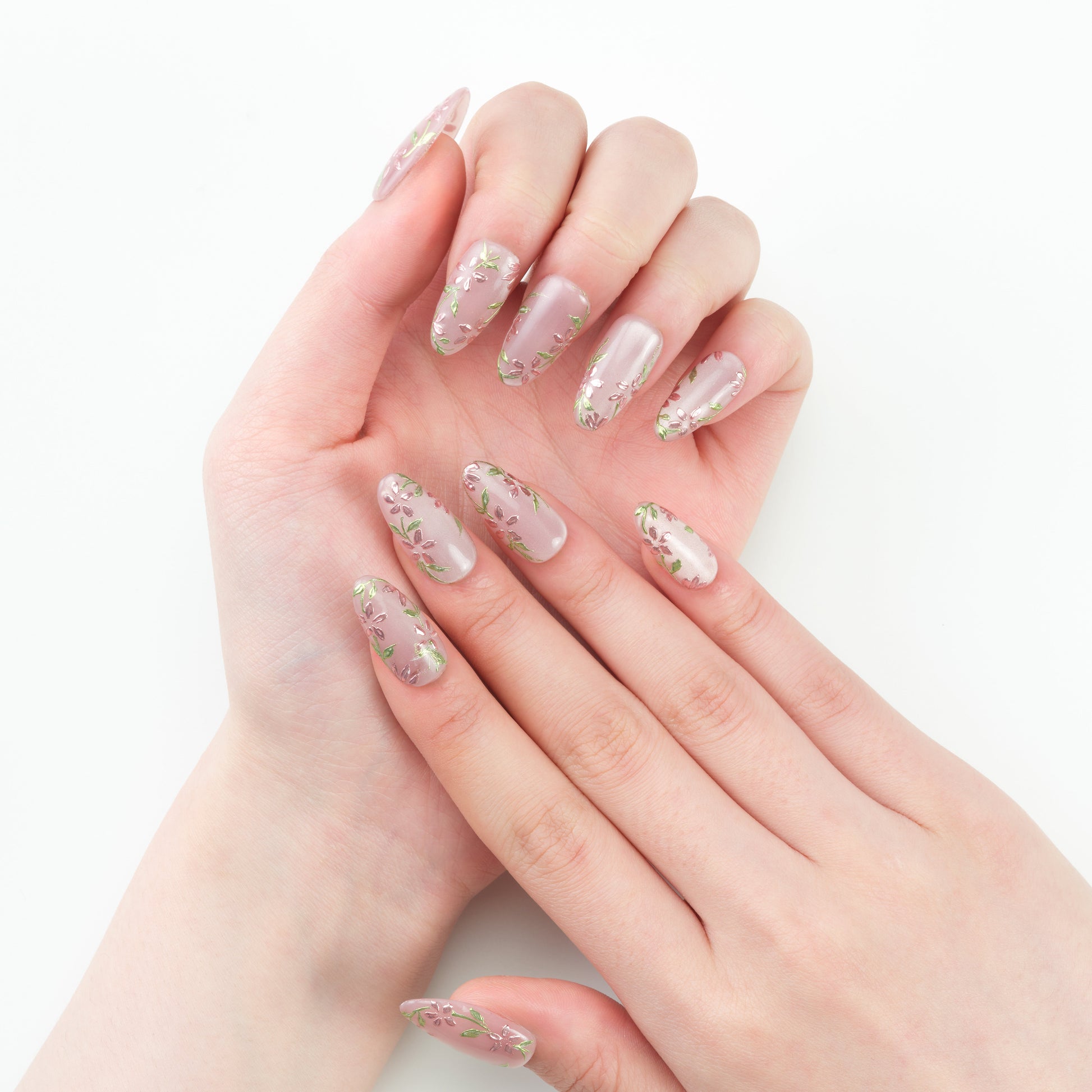 Hand with long, almond-shaped press-on nails featuring pink base and floral designs