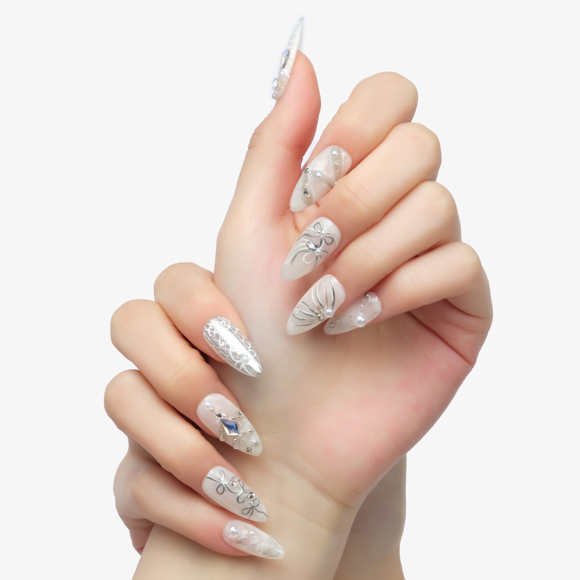 Close-up of hands with long almond-shaped nails featuring white and silver 3D floral and pearl nail art design
