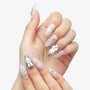 Hand with long almond-shaped press-on nails featuring 3D bunny, pearls, bows, and silver accents