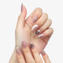 Hand with almond-shaped press-on nails featuring black polka dots and bow nail art on a light pink base.