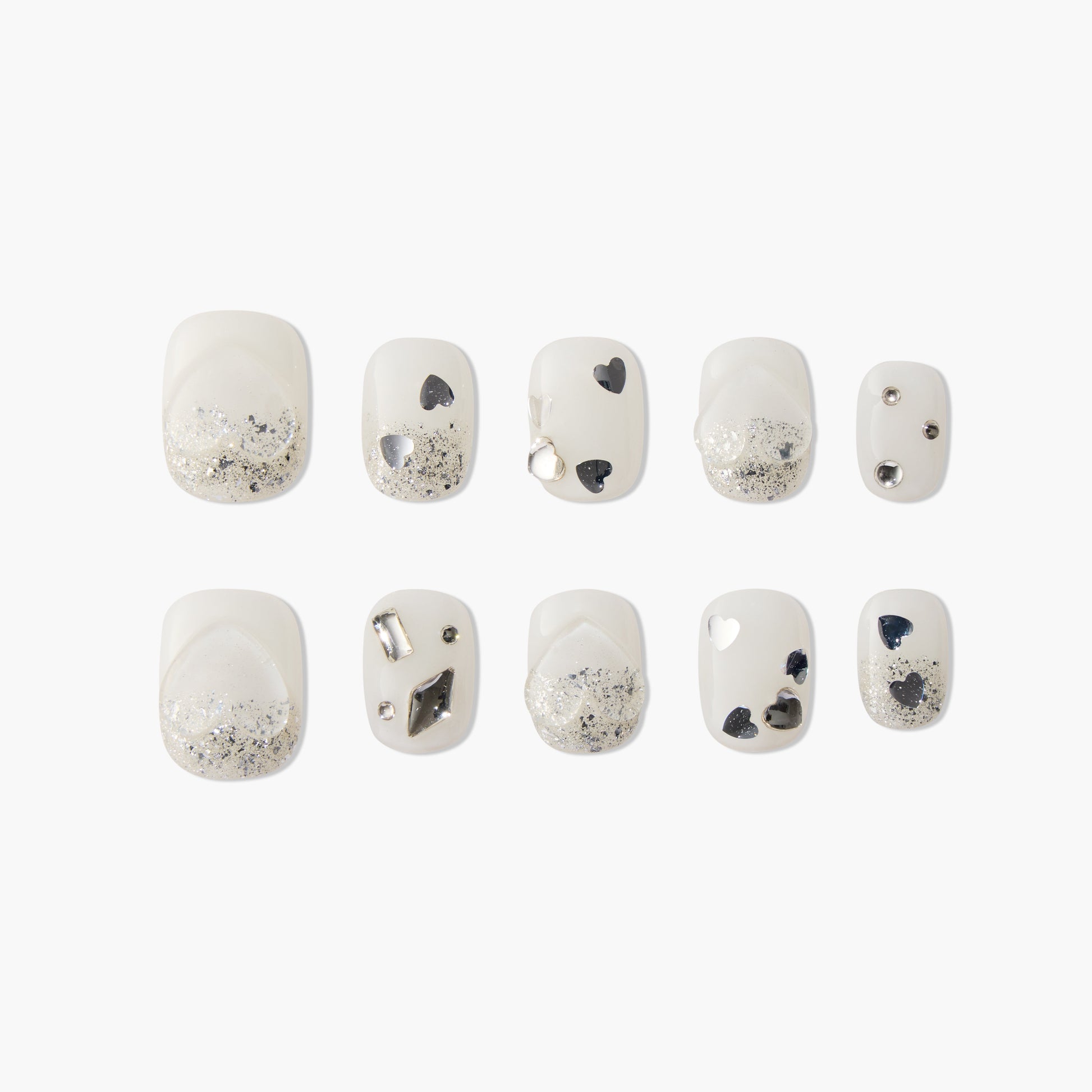 White press-on nails with silver glitter, black heart accents, and metallic embellishments