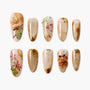 Handmade press-on nails with beige base, floral designs, 3D accents, and gold foil details.