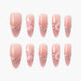 Set of pink ombre press-on nails with heart-shaped and wing embellishments on white background