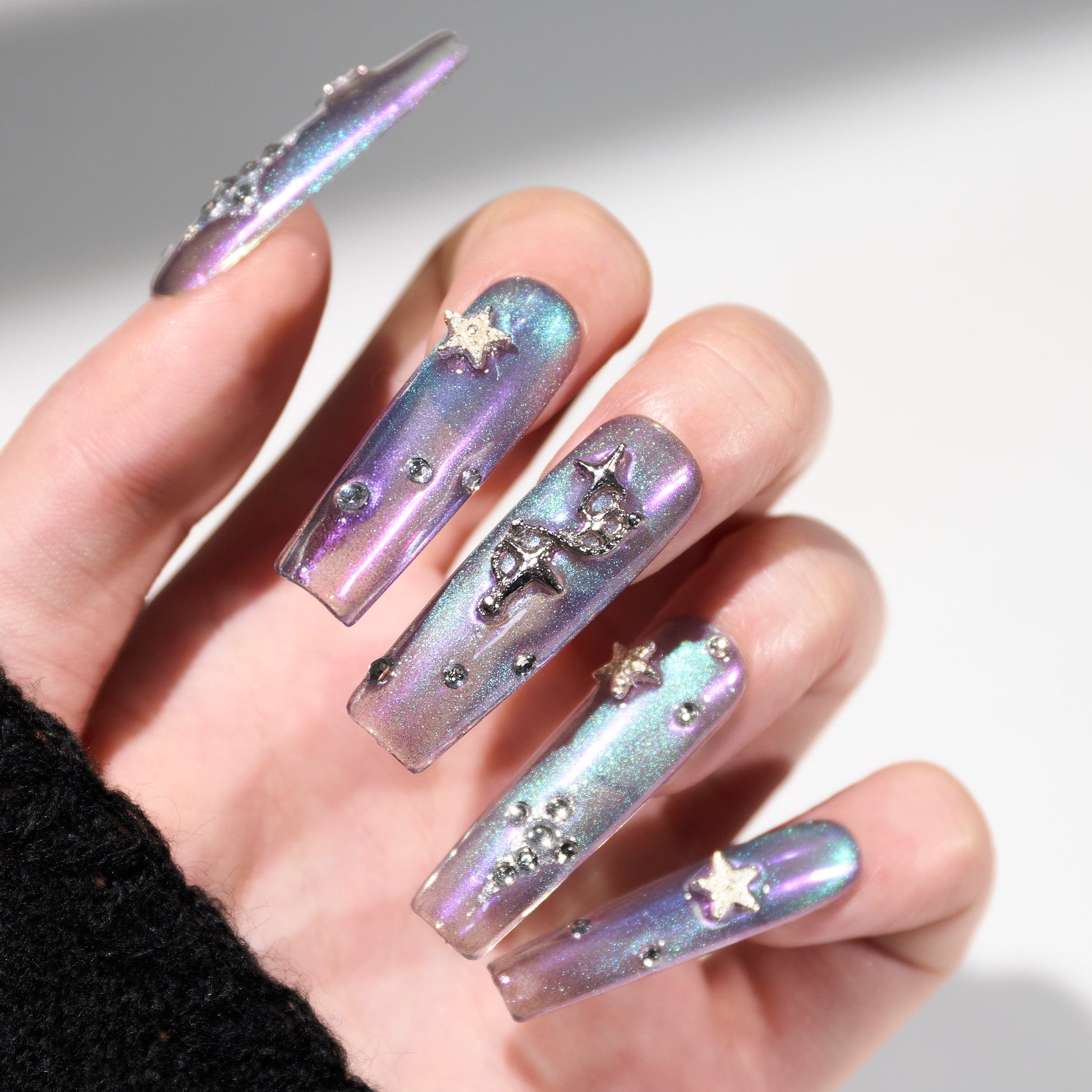 Hand with long iridescent press-on nails featuring star and crystal embellishments