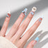 Hand with long pastel blue and white press-on nails featuring bows, star, pearls, and 3D bear design