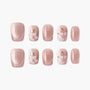 Pink press-on nails with white 3D floral designs and green accents, glossy finish
