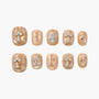 Beige press-on nails with gold cross designs, rhinestones, and pearl accents