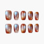 Handmade press-on nails with glossy red, gold, and pearl swirl design on white background