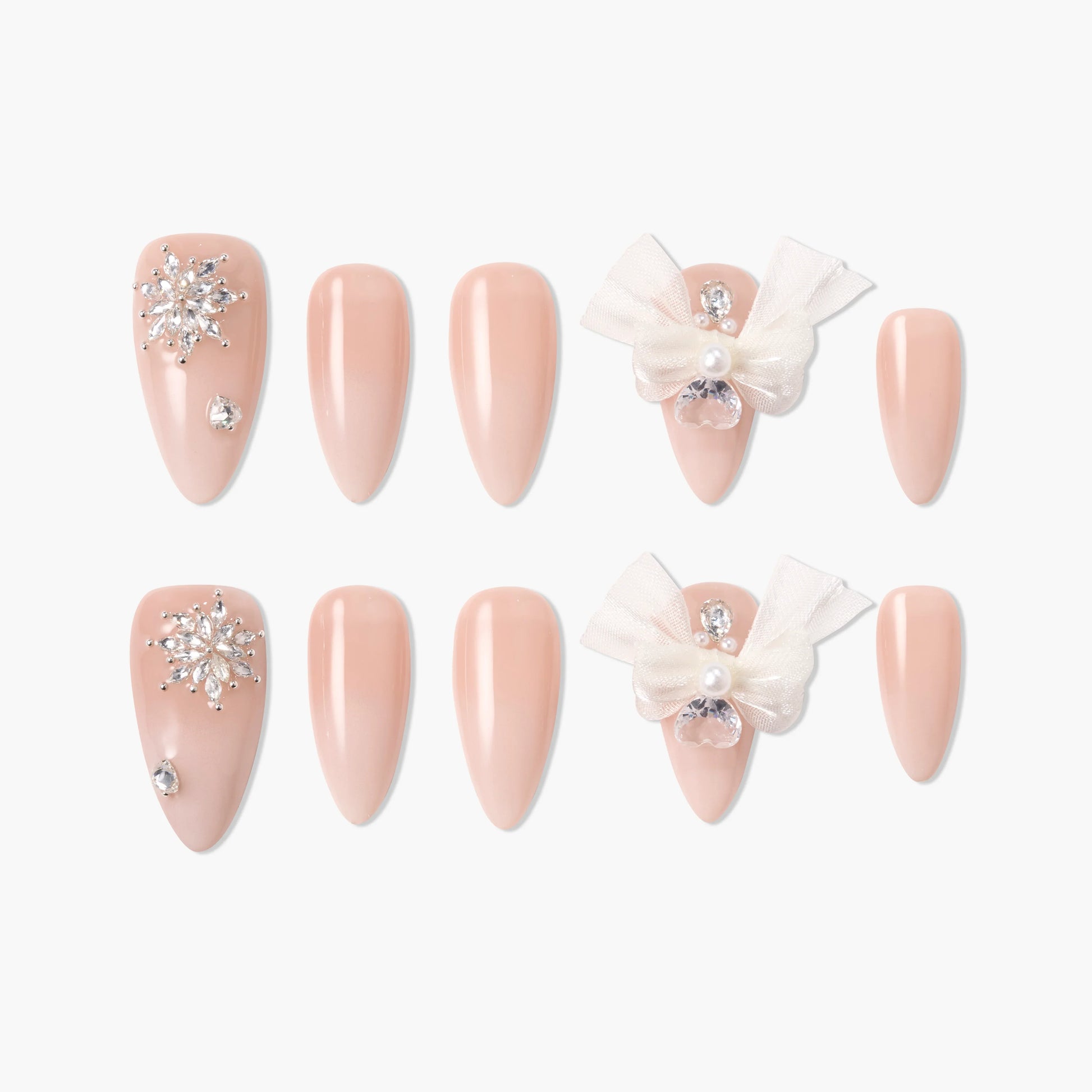 Nude pink press-on nails set with rhinestones, pearl accents, and 3D white bows on a white background