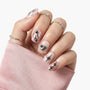 Hand with silver metallic press-on nails featuring 3D accents and geometric designs