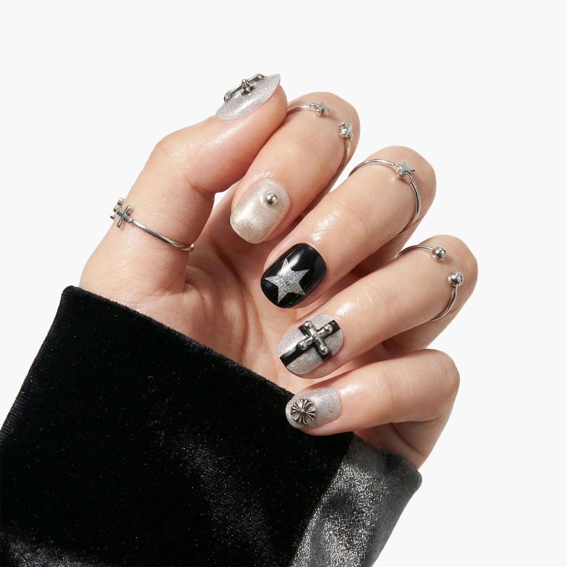 Hand with metallic silver and black press-on nails featuring star and cross designs, adorned with silver rings.