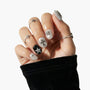Hand with silver glitter press-on nails featuring 3D star and cross charms, black accent nail.