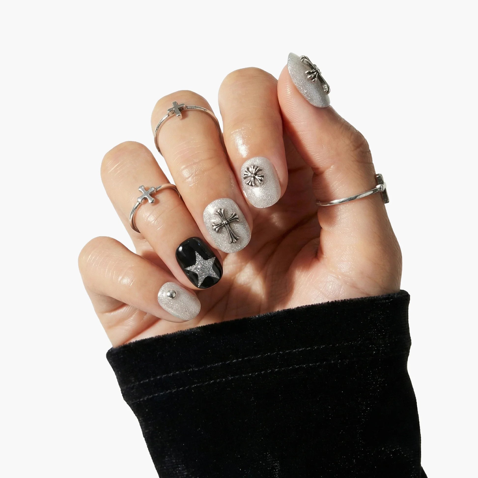 Hand with silver glitter press-on nails featuring 3D star and cross charms, black accent nail.