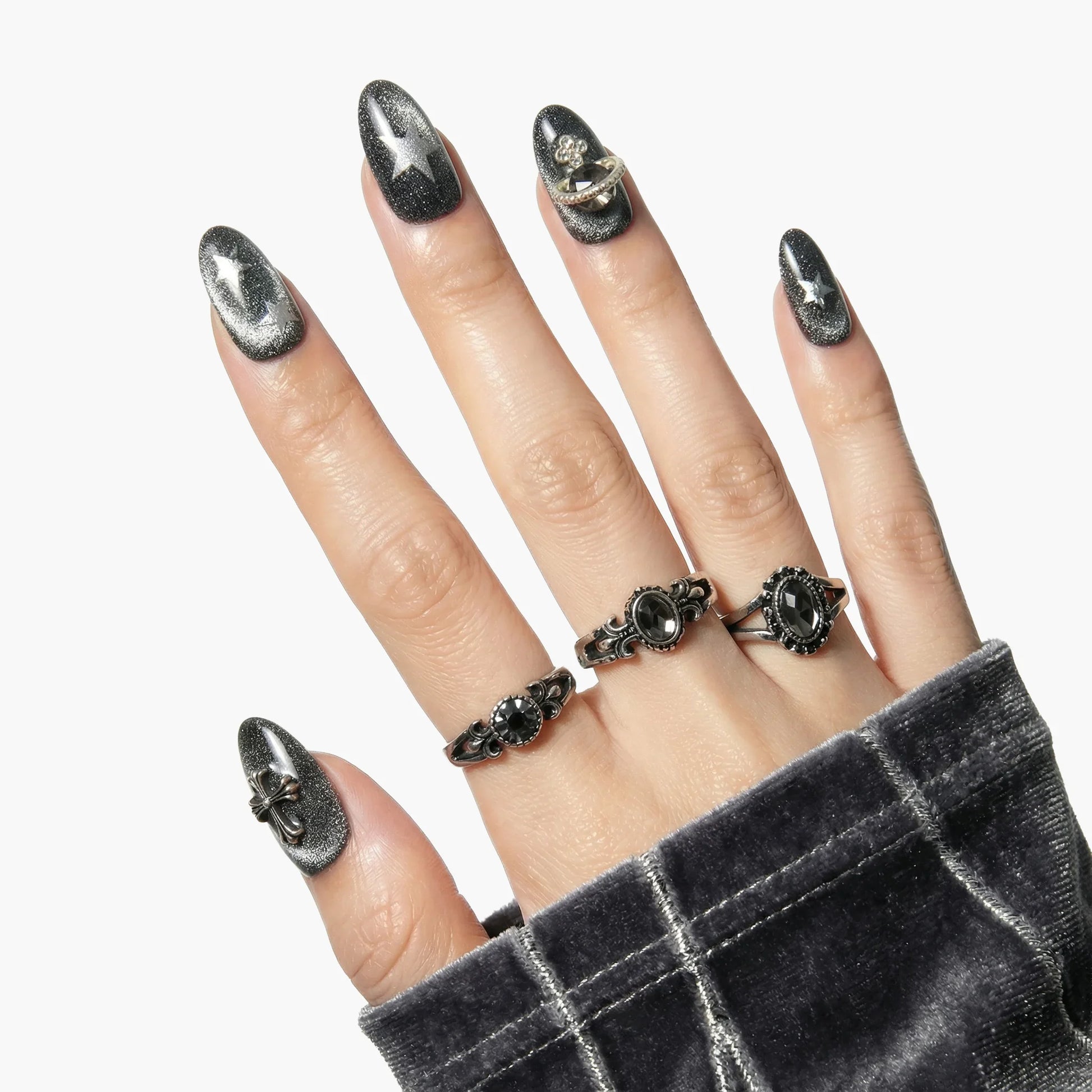 Hand with long, metallic silver press-on nails featuring star patterns and rhinestone rings