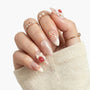 Hand with long almond-shaped press-on nails featuring pink and white 3D floral designs and pearls.