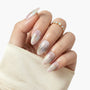 Hand with long almond-shaped press-on nails in pearl white with gold flakes, elegant nail art
