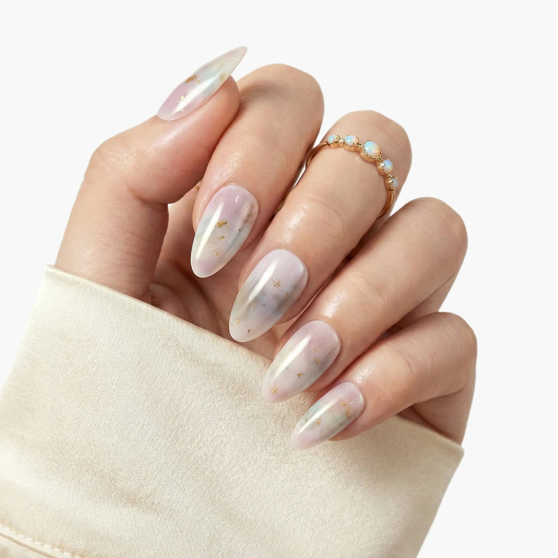 Hand with long almond-shaped press-on nails in pearl white with gold flakes, elegant nail art