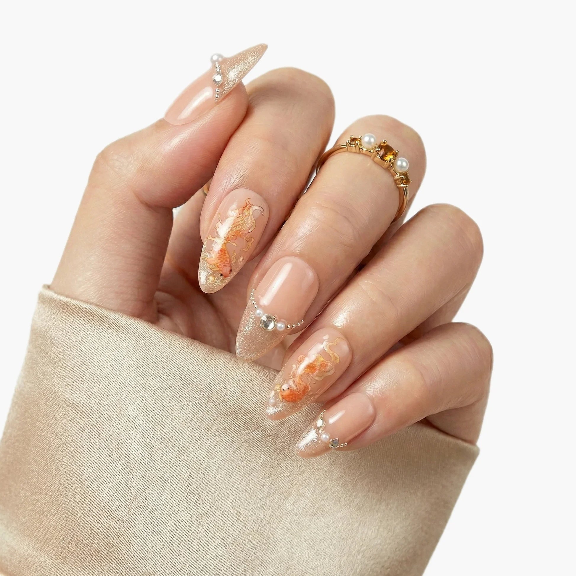 Hand with elegant press-on nails featuring gold koi fish art, pearls, and glitter tips