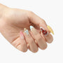 Hand with multicolored handmade press-on nails featuring 3D bows, swirls, and playful designs.