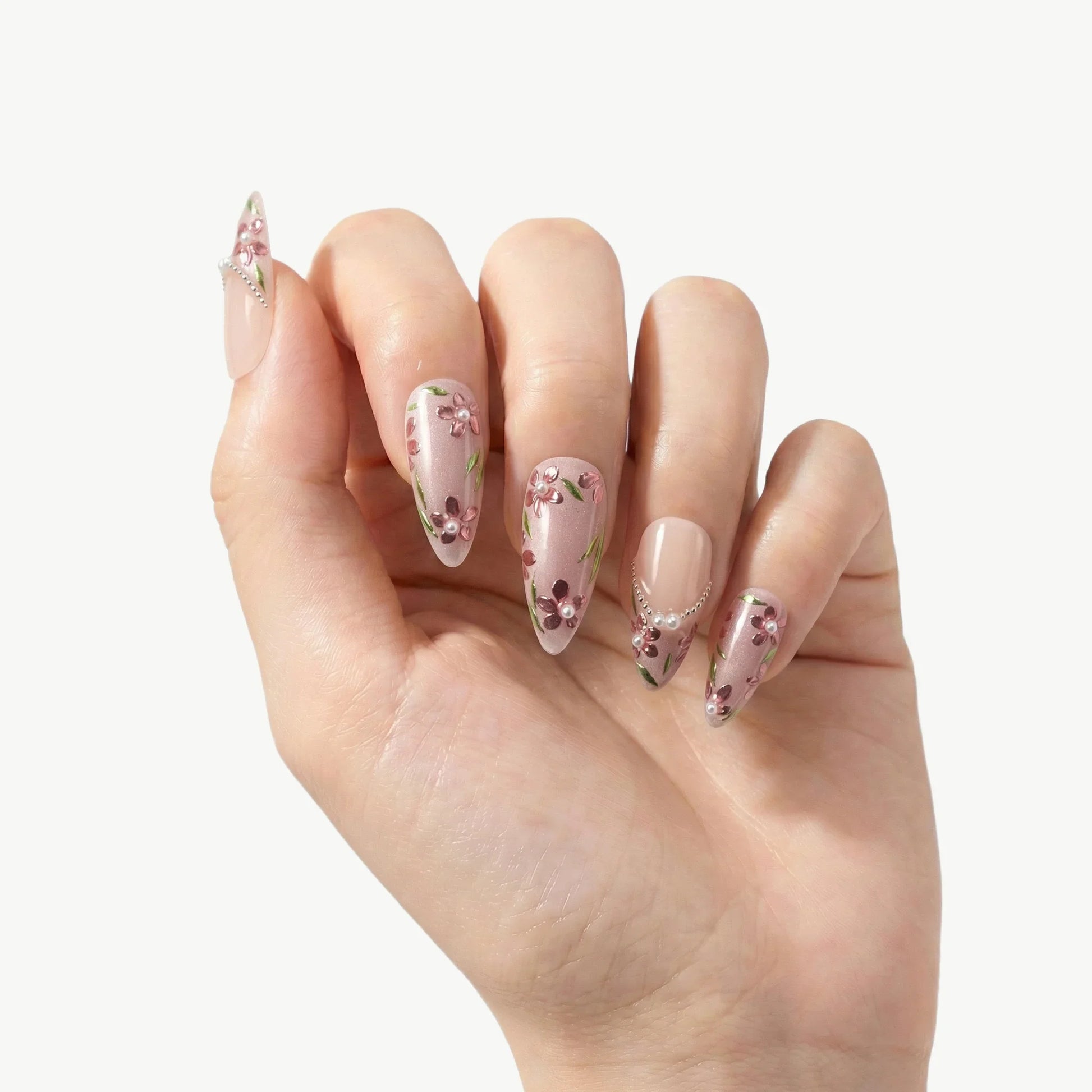 Hand with long almond-shaped press-on nails featuring pink 3D floral designs and rhinestones