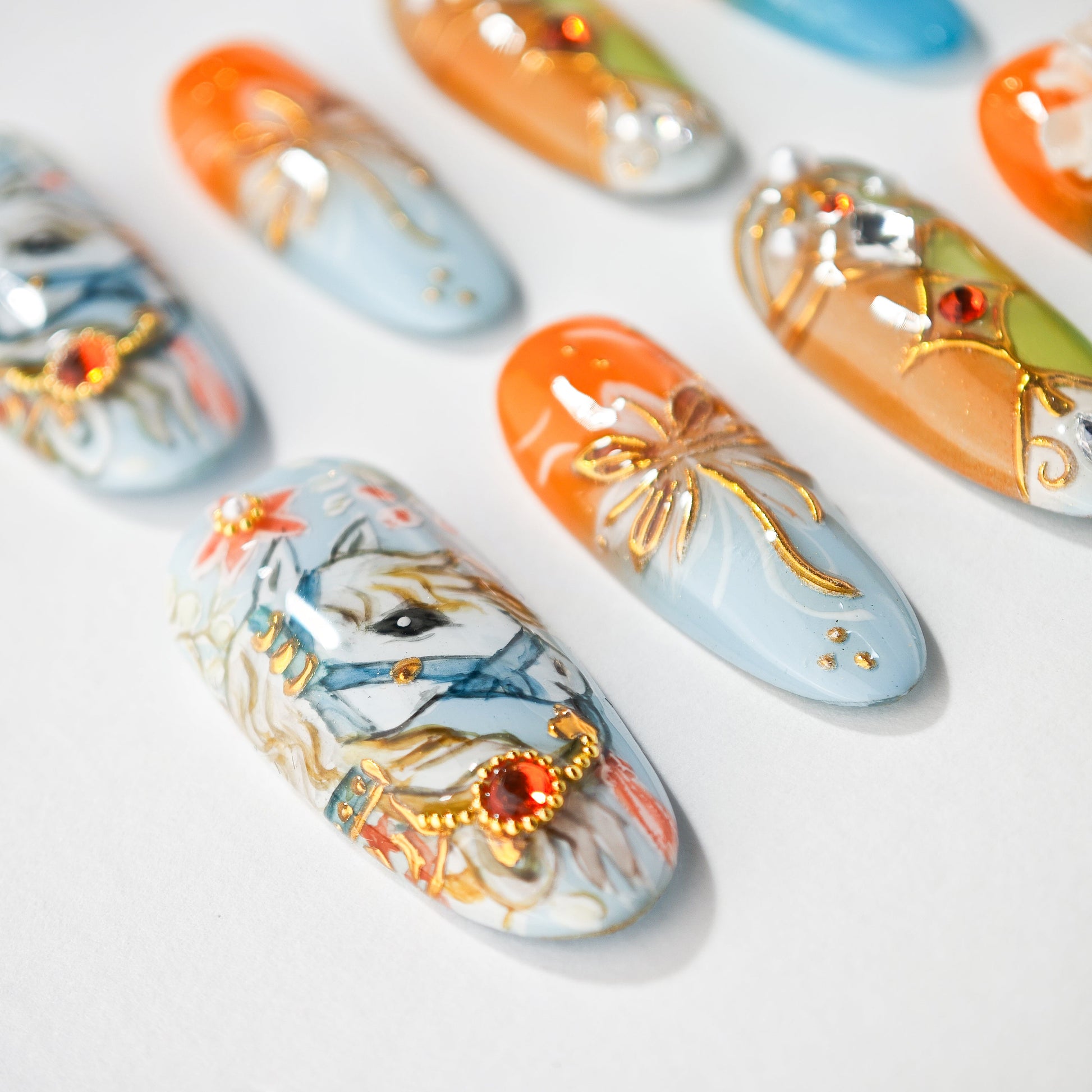 Set of decorated artificial nails with horse and floral gold accent designs on white surface