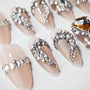 Nude almond press-on nails with large rhinestone and gem embellishments