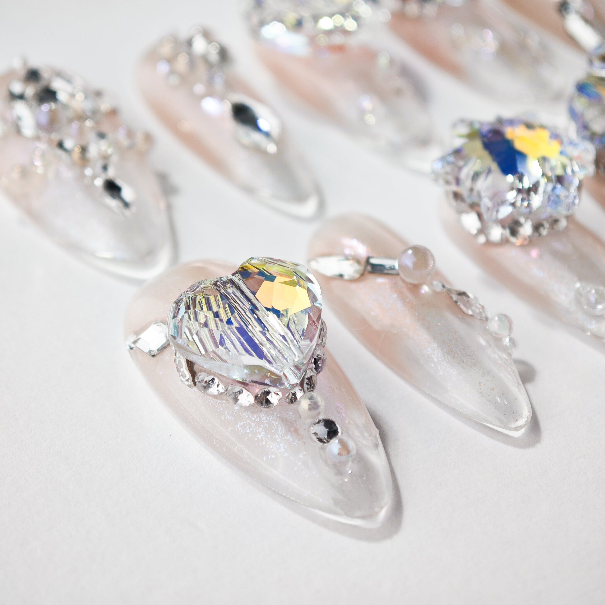Close-up of clear acrylic nails with large heart-shaped crystal and small rhinestones on a white background