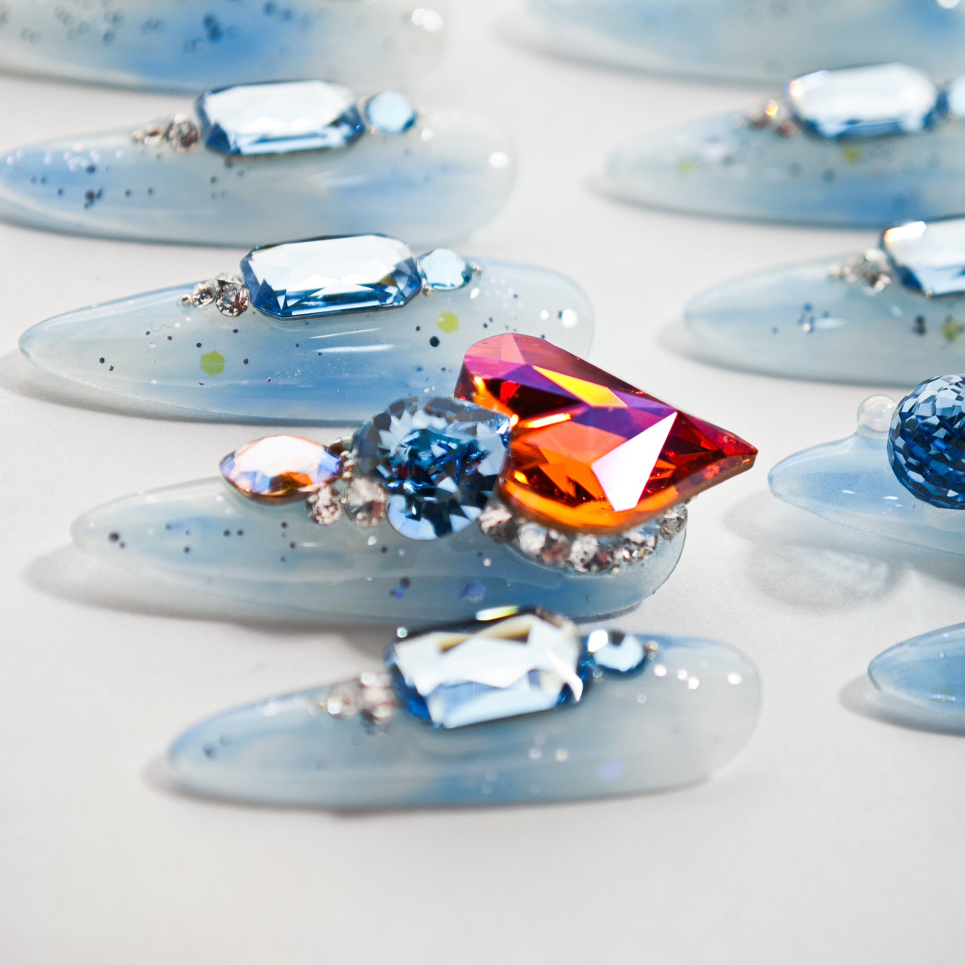 Close-up of blue translucent fake nails decorated with large colorful rhinestones and glitter