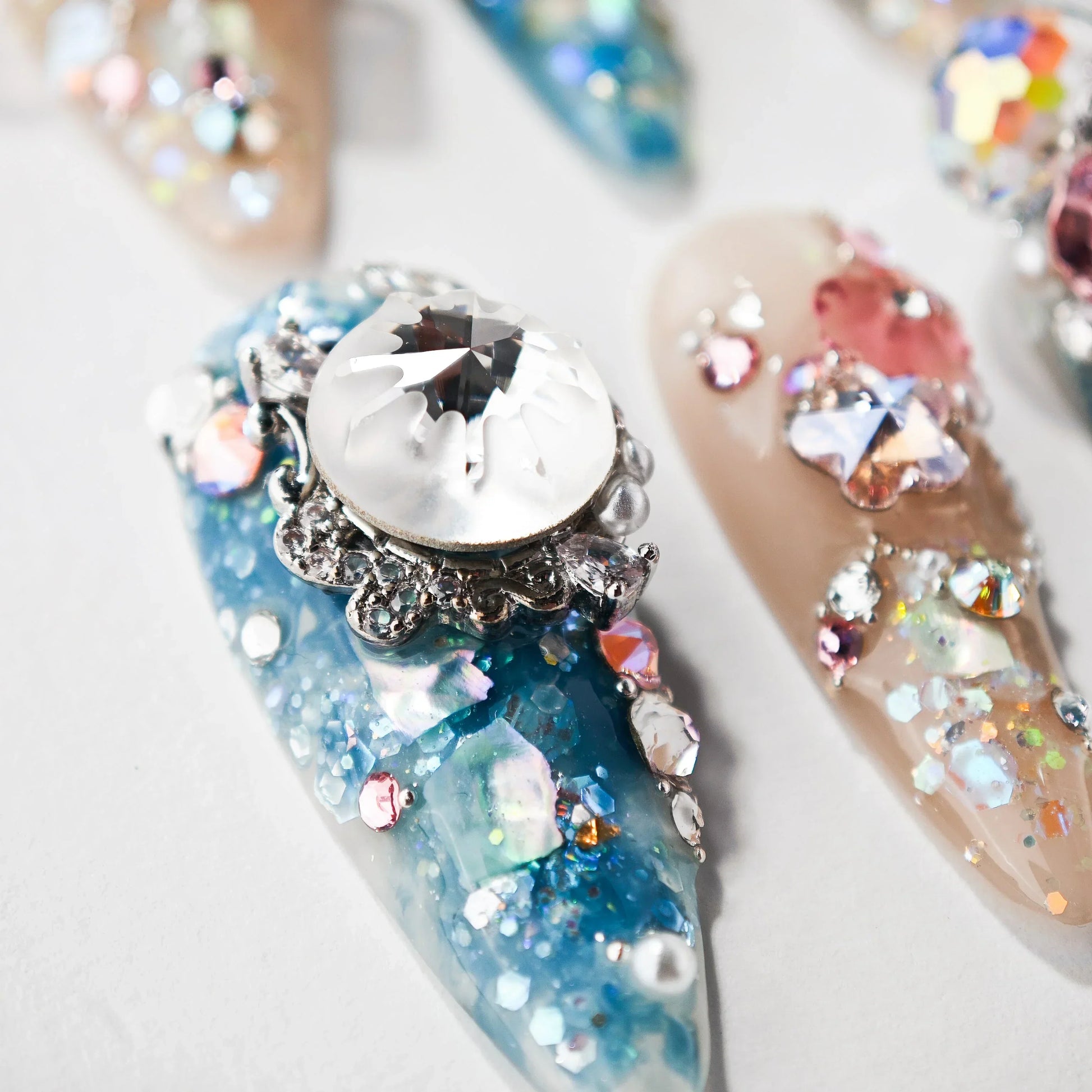 Close-up of jeweled blue and nude acrylic nail art with rhinestones and metallic embellishments