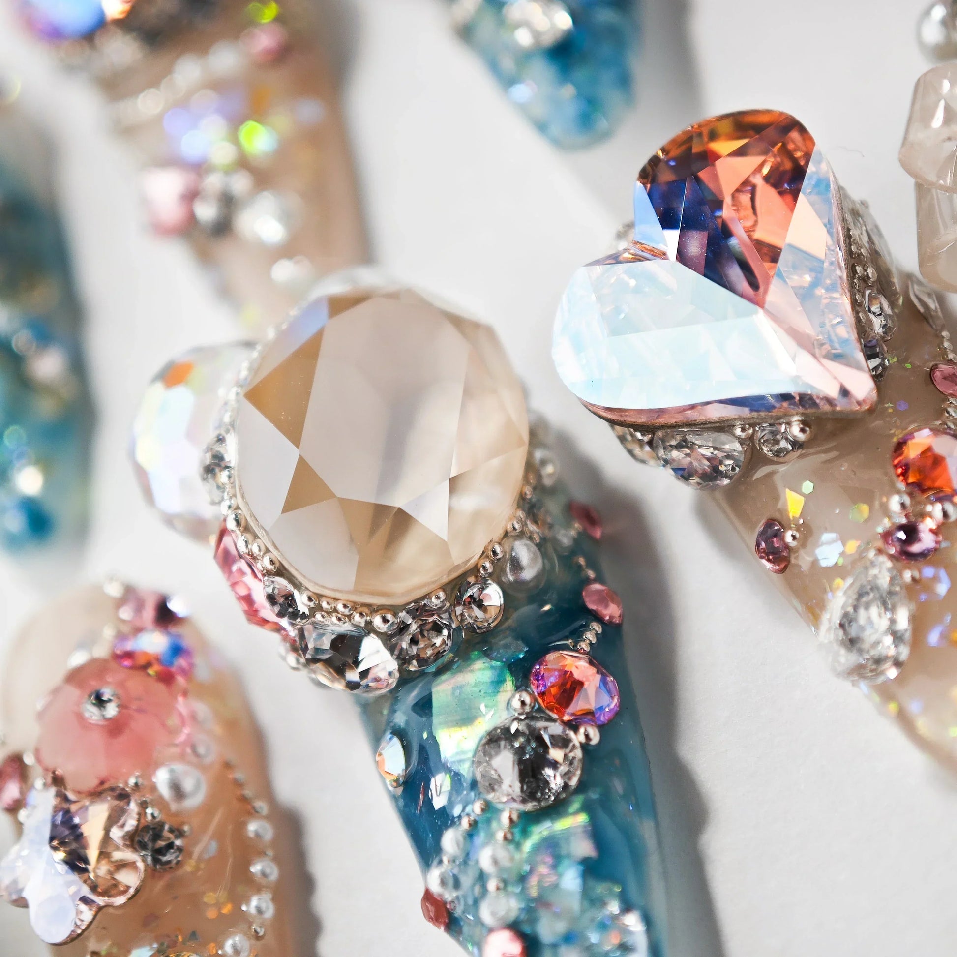 Close-up of decorative long artificial nails with large crystal and heart-shaped rhinestones on blue and beige backgrounds