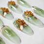 Green handmade press-on nails with 3D orange floral art and gold foil accents on white background