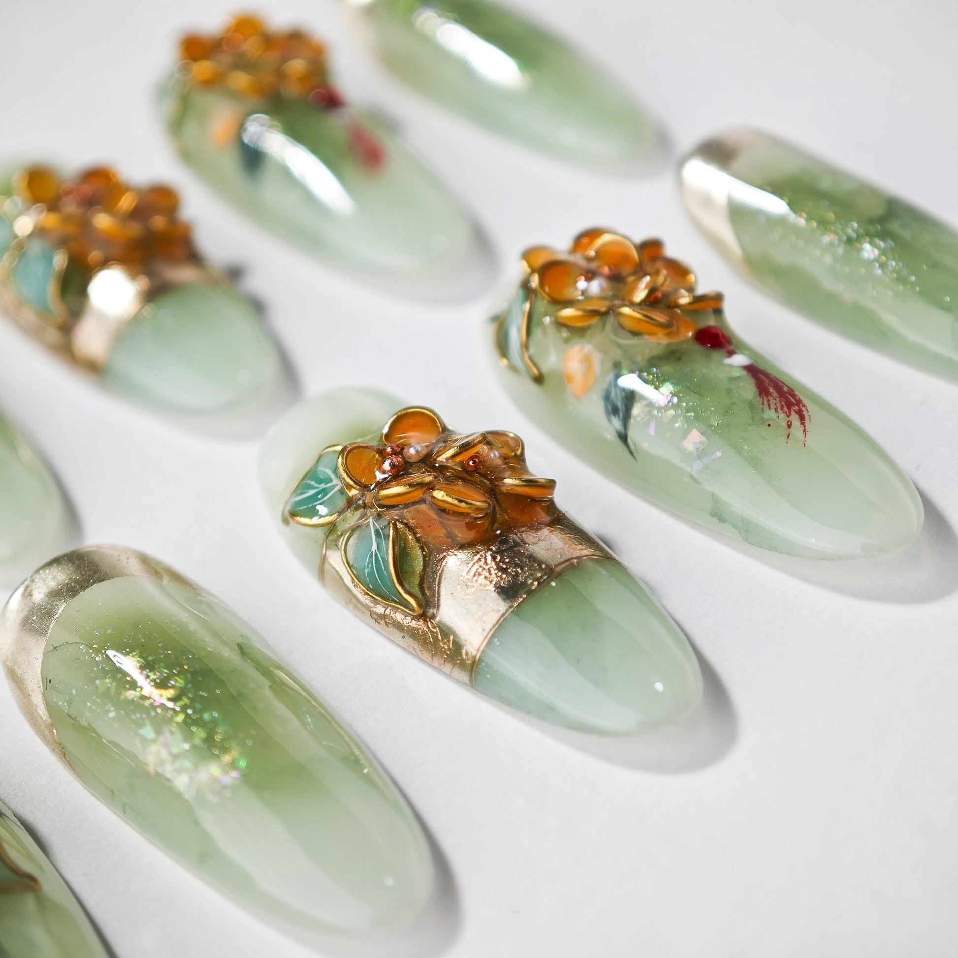Close-up of green and gold floral decorative artificial nails on white background