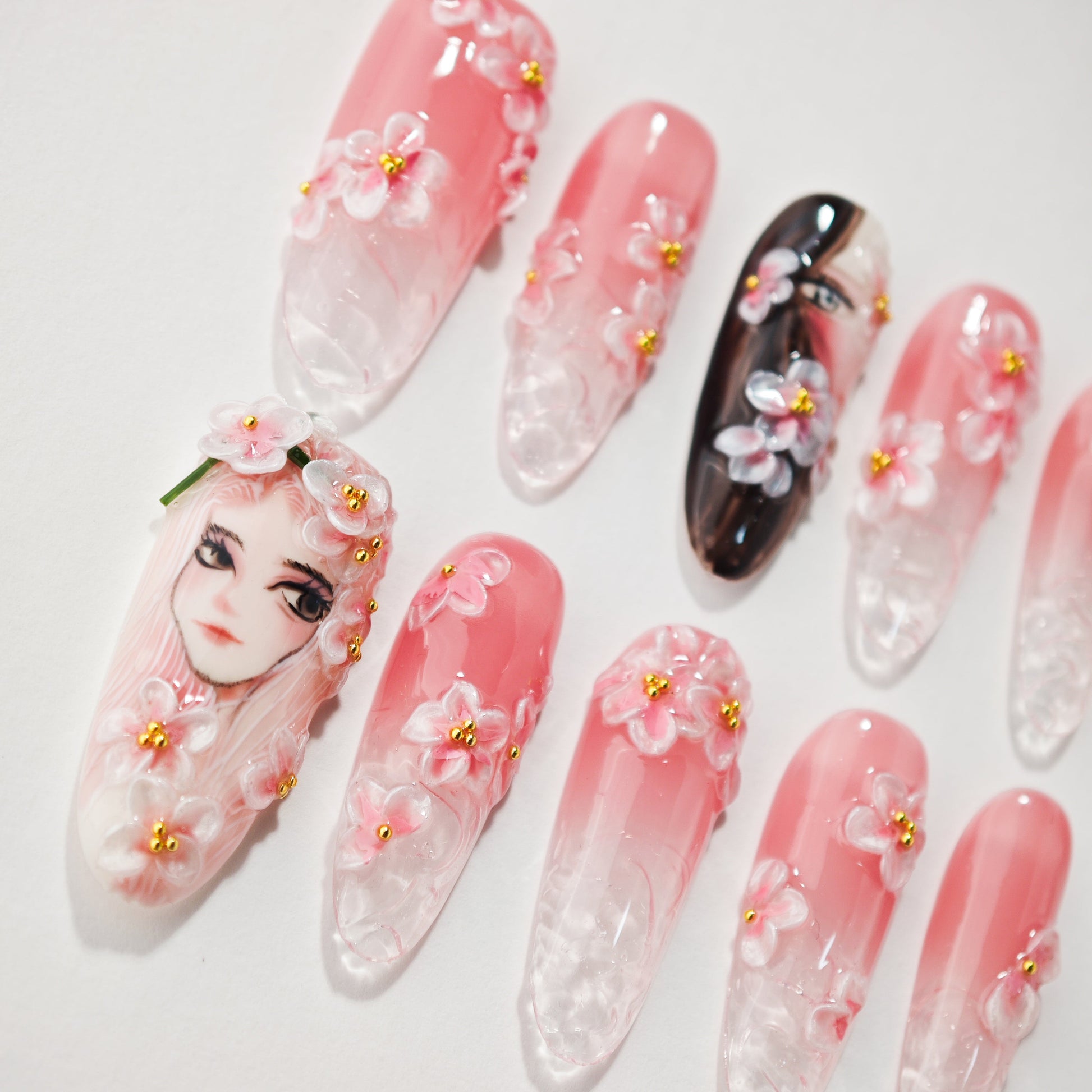 Set of pink and clear acrylic nails with 3D floral designs and detailed face art on two nails