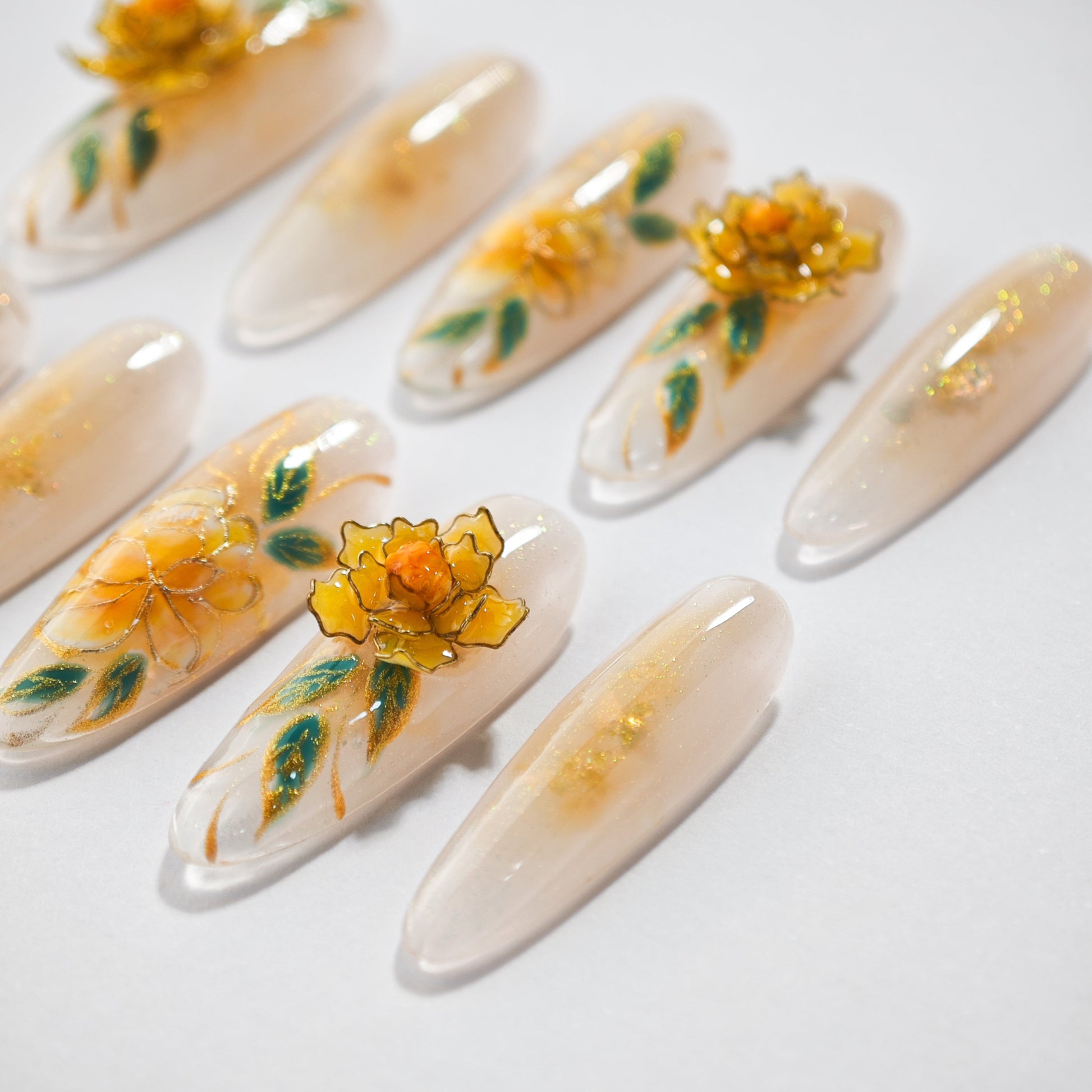 Set of artificial long nails with yellow flower and green leaf designs on a light background