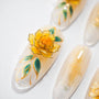 Handmade press-on nail with 3D yellow flower and green leaves on glossy nude base
