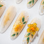 Handmade press-on nails with yellow floral designs and green leaf accents on a nude base