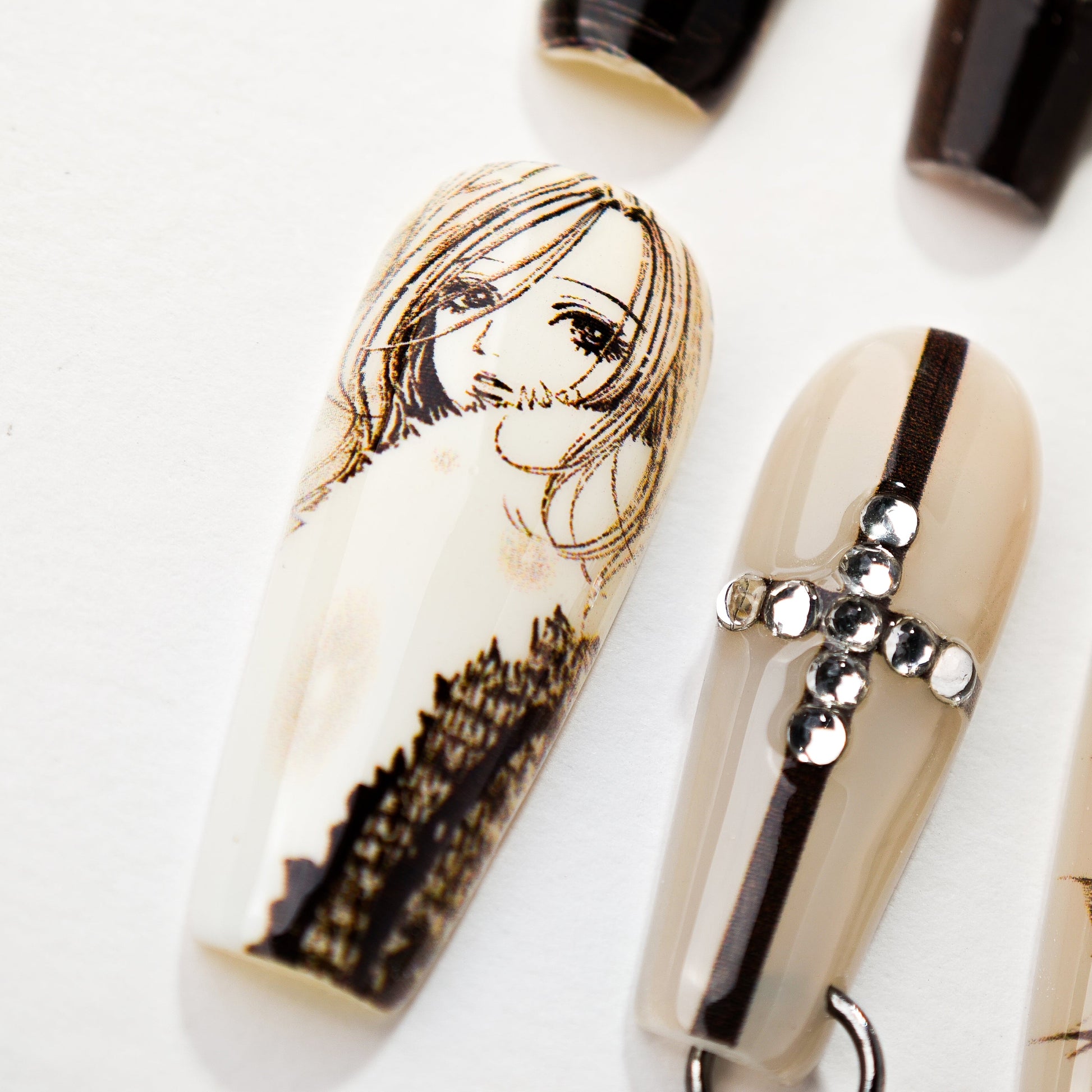 Close-up of detailed nail art featuring a woman's face sketch and rhinestone cross design