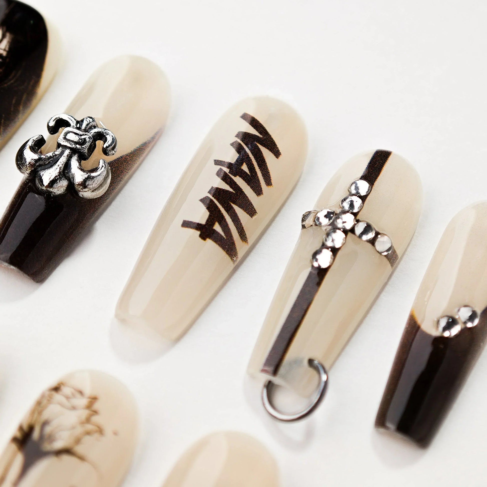 Set of beige and black acrylic nails with 3D silver fleur-de-lis, rhinestones, cross, and text nail art