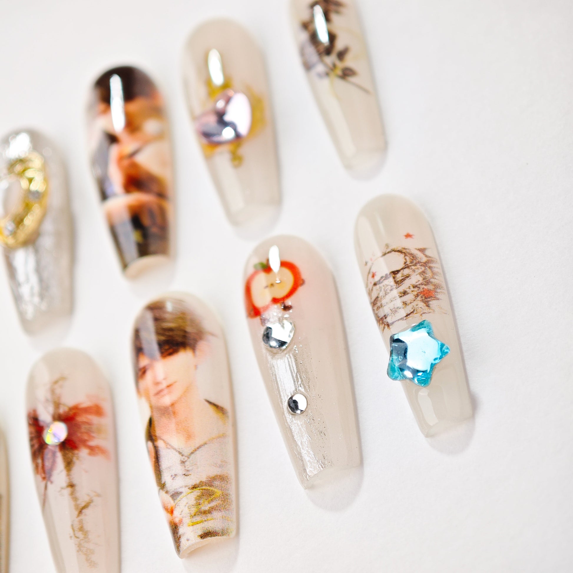 Transparent artificial nails with decorative designs including portraits, hearts, flowers, and blue star embellishments