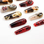 Handmade press-on nails with red floral designs, art prints, and rhinestone accents on white background